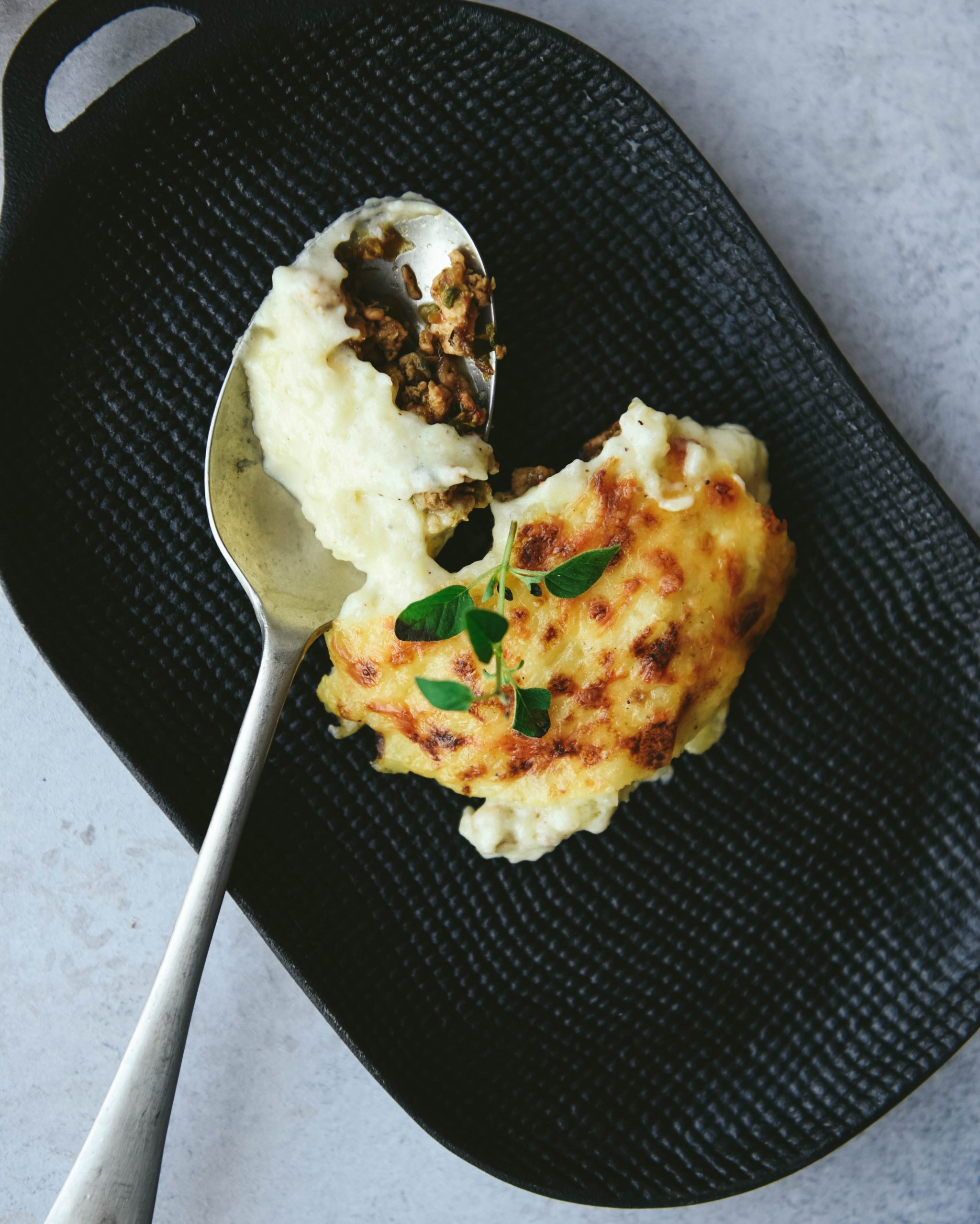 Top shot of black plate, spoon and deconstructed Spicy Shepherd's pie